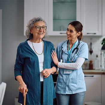 Happy home caregiver assisting her senior patient with walking through the kitchen